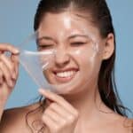 woman removing with hardness her facial mask and smiling