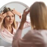 Woman stares in the mirror looking at unwanted wrinkles that have appeared on her forehead despite moisturizing