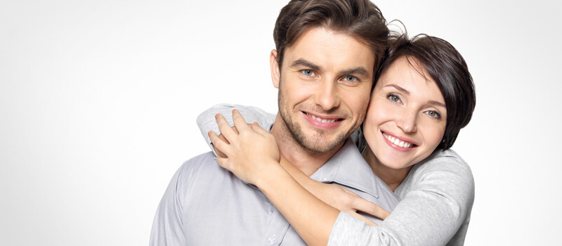Woman hugging man from behind while both are smiling against white background