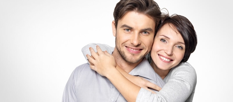 Woman hugging man from behind while both are smiling against white background